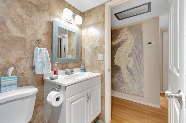 bathroom with tile walls, wood finished floors, toilet, vanity, and baseboards