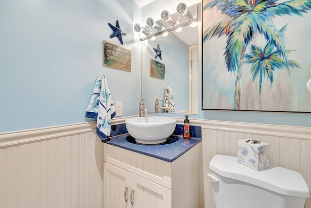 half bathroom with wainscoting, vanity, and toilet