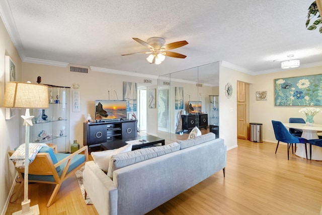 living area with a textured ceiling, light wood-style floors, ceiling fan, ornamental molding, and baseboards