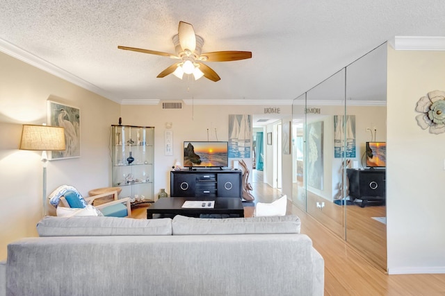 living area featuring wood finished floors, ornamental molding, a textured ceiling, and ceiling fan