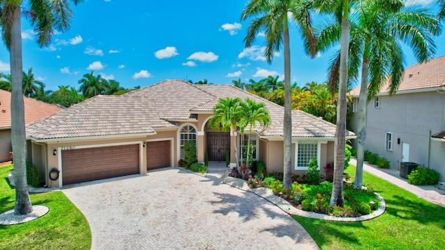 mediterranean / spanish-style house with a tile roof, a garage, decorative driveway, and stucco siding