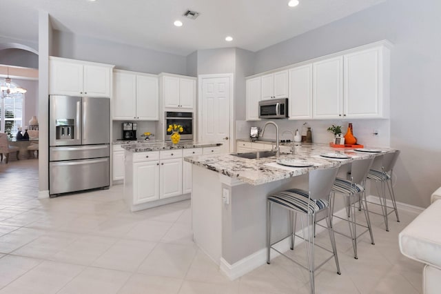 kitchen with stainless steel appliances, a sink, a peninsula, light stone countertops, and white cabinetry