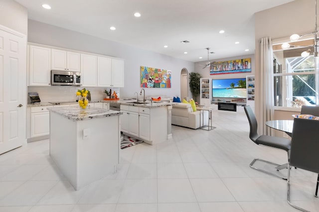 kitchen with stainless steel microwave, a sink, a center island, arched walkways, and recessed lighting