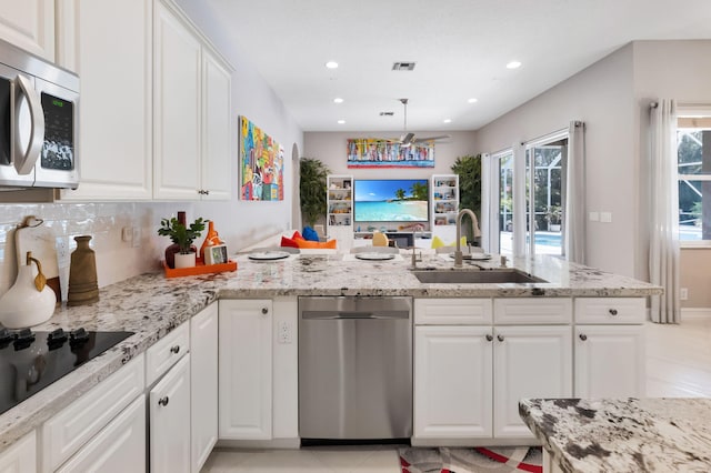 kitchen featuring a sink, appliances with stainless steel finishes, a peninsula, white cabinetry, and light stone countertops
