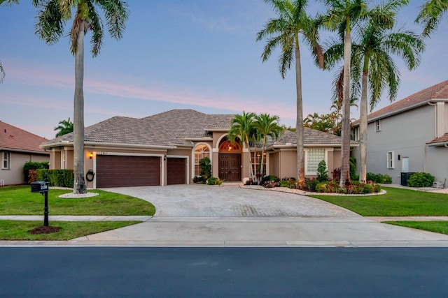 view of front of home featuring decorative driveway, an attached garage, a front yard, stucco siding, and a tiled roof