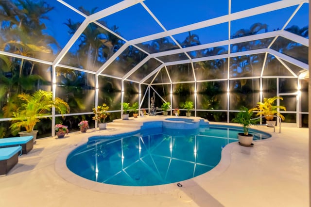 pool at twilight featuring a patio area, a pool with connected hot tub, and glass enclosure