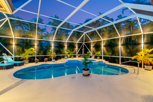 pool at night featuring an outdoor hot tub, a patio area, an outdoor pool, and glass enclosure