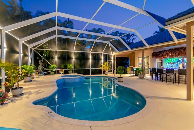 pool at twilight with a patio area, a lanai, and a pool with connected hot tub