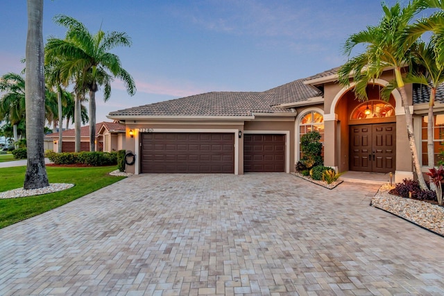 mediterranean / spanish home featuring driveway, a garage, stucco siding, a tile roof, and a front lawn