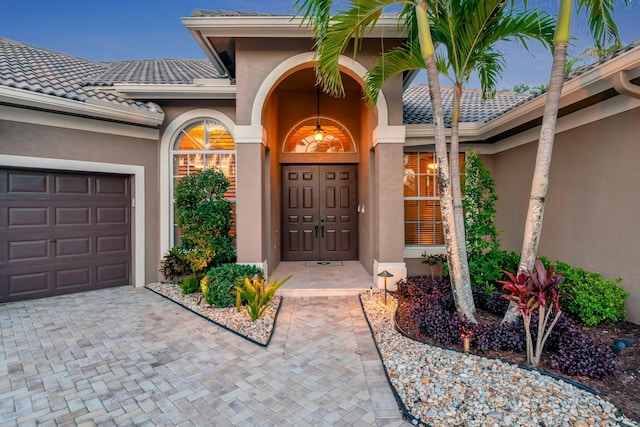 doorway to property with stucco siding, a tile roof, and an attached garage