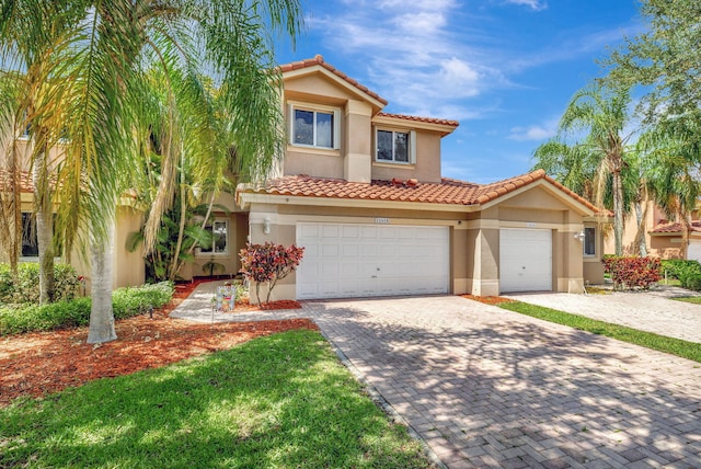 mediterranean / spanish home with a tiled roof, stucco siding, decorative driveway, and a garage