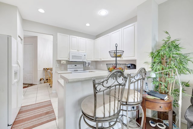 kitchen with white appliances, light countertops, white cabinetry, a kitchen bar, and light tile patterned floors