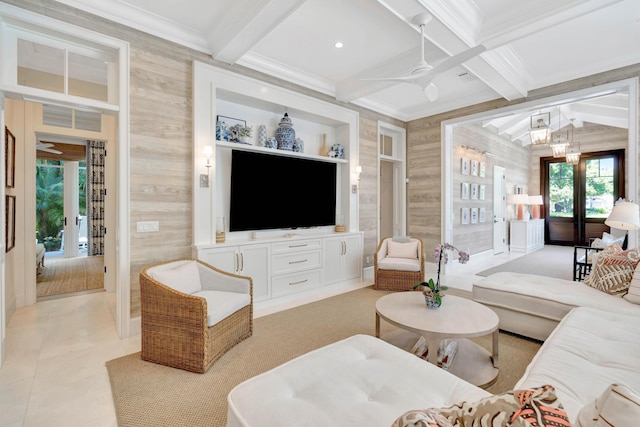 living room featuring ornamental molding, beamed ceiling, a ceiling fan, wood walls, and a chandelier