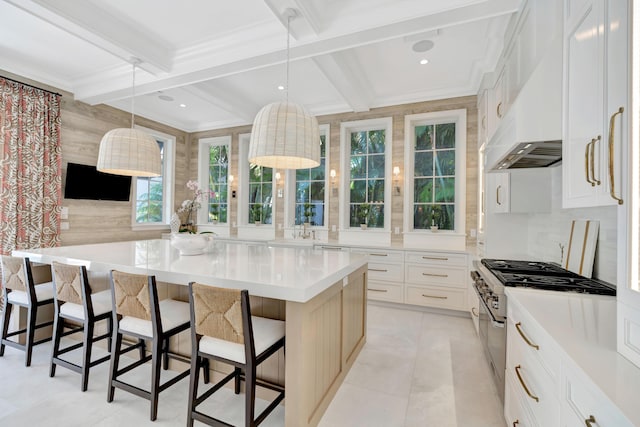 kitchen featuring stainless steel stove, crown molding, a breakfast bar, beamed ceiling, and light countertops