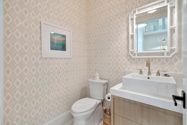 bathroom featuring toilet, wallpapered walls, and vanity