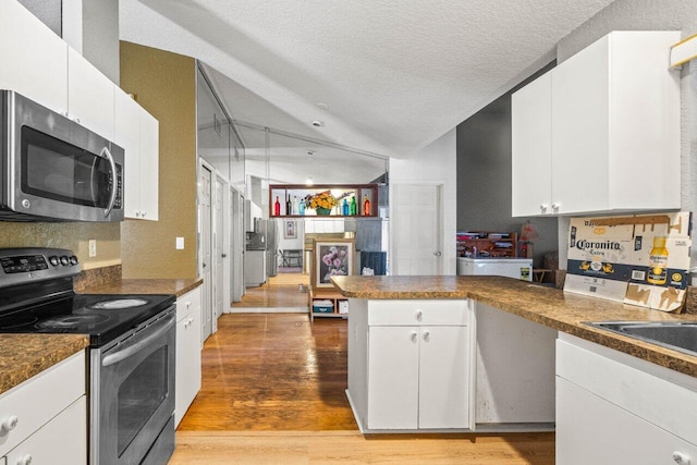 9023 Seminole Pratt Whitney Rd, The Acreage, FL 33470 - kitchen with appliances with stainless steel finishes, a peninsula, light wood finished floors, white cabinetry, and a textured ceiling