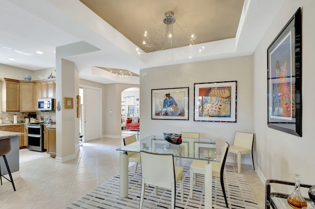 dining space with arched walkways, light tile patterned floors, a chandelier, a raised ceiling, and recessed lighting