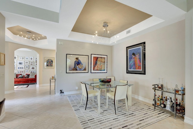 dining room featuring a tray ceiling, arched walkways, light tile patterned floors, and a chandelier