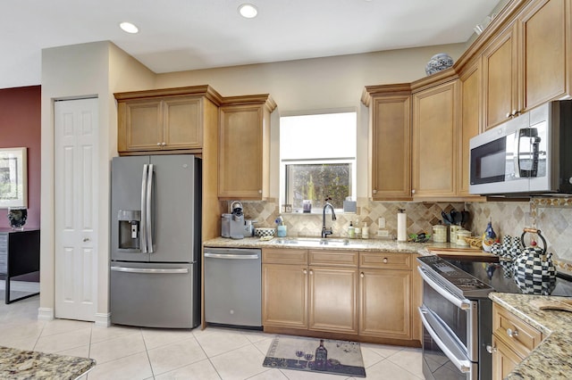 kitchen with appliances with stainless steel finishes, a sink, light tile patterned flooring, light stone countertops, and tasteful backsplash