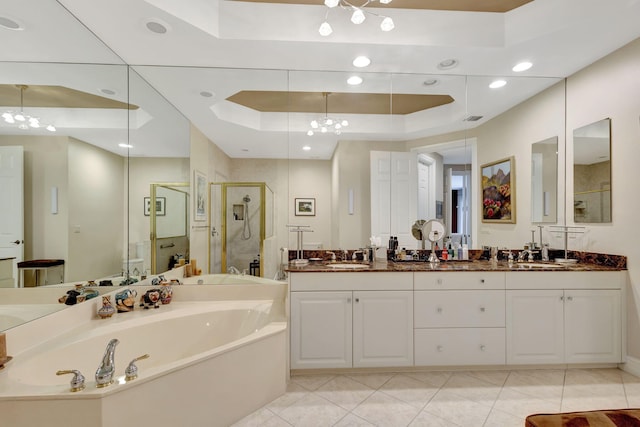 bathroom with a raised ceiling, a stall shower, a garden tub, a chandelier, and double vanity