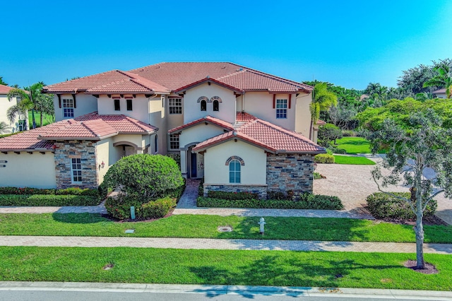 mediterranean / spanish-style house featuring stucco siding, stone siding, a tiled roof, and a front yard
