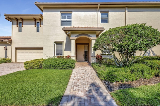 view of front of home with an attached garage, stucco siding, driveway, a front lawn, and a tiled roof