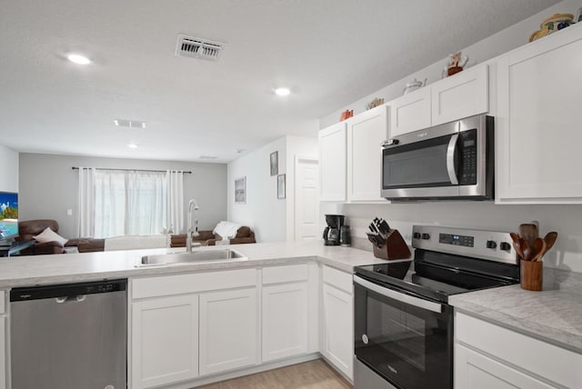 kitchen with stainless steel appliances, a sink, open floor plan, light countertops, and recessed lighting
