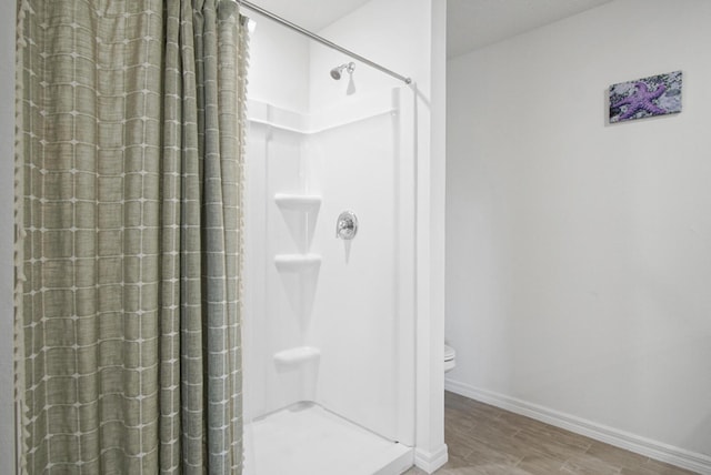 full bath featuring a shower stall, wood finished floors, baseboards, and toilet