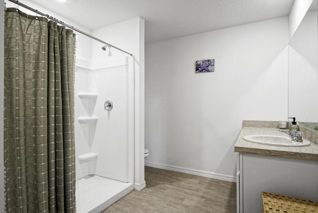 full bath with a shower stall, vanity, a textured ceiling, toilet, and baseboards