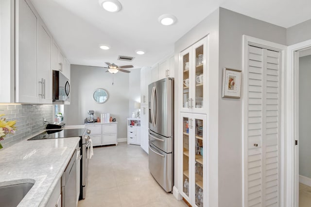 kitchen with stainless steel appliances, white cabinets, tasteful backsplash, glass insert cabinets, and light stone counters