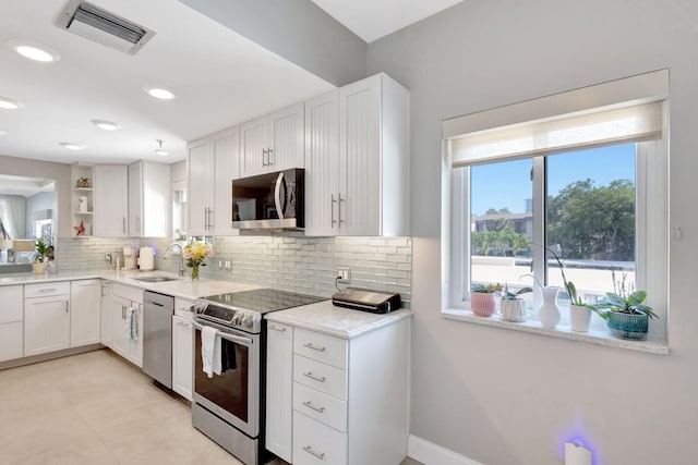 kitchen featuring stainless steel appliances, a sink, open shelves, backsplash, and white cabinets