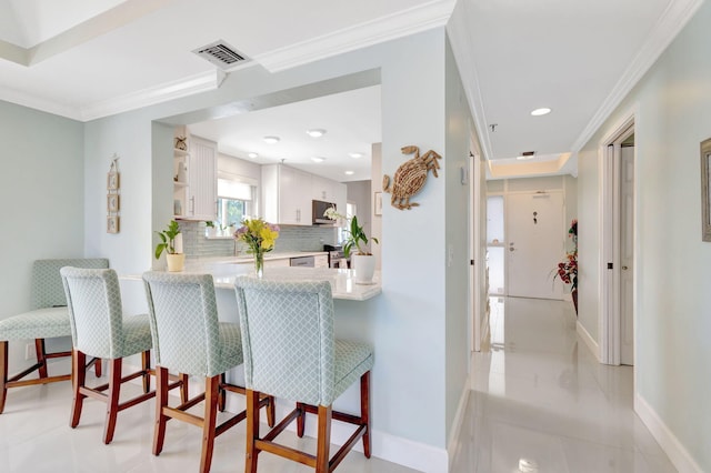 kitchen with baseboards, ornamental molding, a kitchen breakfast bar, light countertops, and decorative backsplash