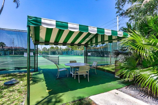 view of patio featuring a tennis court and fence