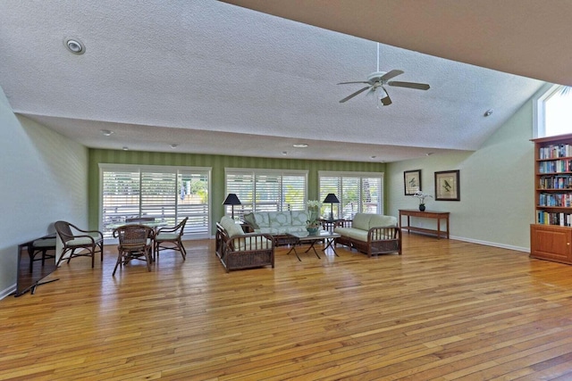 living area featuring a textured ceiling, light wood-style flooring, ceiling fan, lofted ceiling, and baseboards