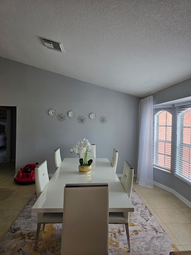 dining space with a textured ceiling, light tile patterned floors, and baseboards