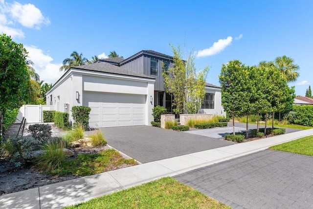 view of front facade featuring an attached garage, decorative driveway, stucco siding, fence, and a gate
