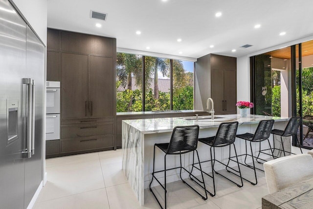 kitchen with built in fridge, modern cabinets, a kitchen bar, a sink, and light stone countertops