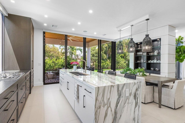 kitchen with a sink, stainless steel gas stovetop, a kitchen island with sink, recessed lighting, and light stone counters