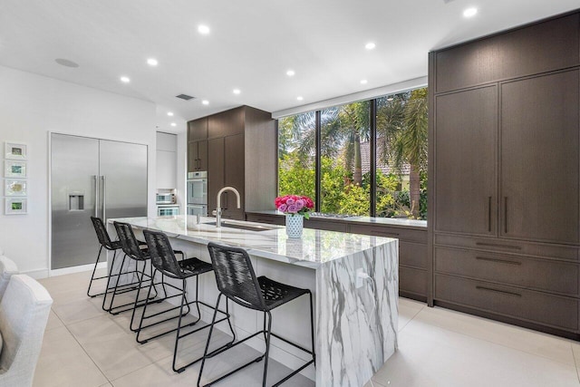 kitchen featuring a sink, appliances with stainless steel finishes, a large island, a breakfast bar area, and light stone countertops