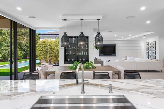 kitchen featuring a sink, light stone counters, recessed lighting, hanging light fixtures, and expansive windows