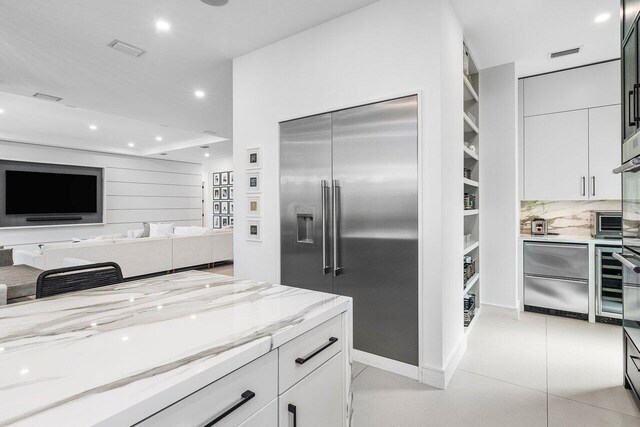 kitchen featuring appliances with stainless steel finishes, light stone counters, recessed lighting, light tile patterned floors, and white cabinets
