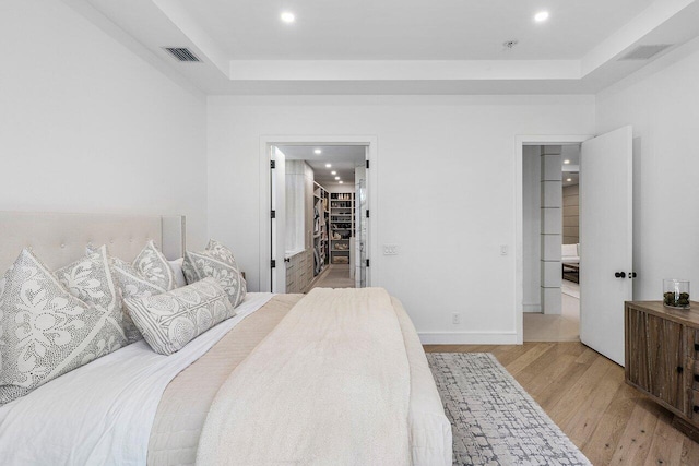bedroom with a tray ceiling, light wood-type flooring, recessed lighting, and a spacious closet