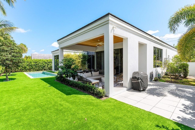 rear view of house with ceiling fan, stucco siding, a lawn, and a patio