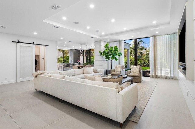 living room with a tray ceiling, a barn door, recessed lighting, light tile patterned flooring, and expansive windows