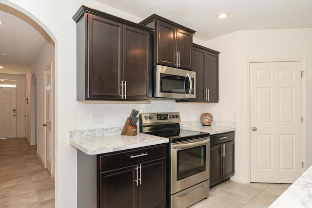 567 SW Paar Dr, Port Saint Lucie, FL 34953 - kitchen with appliances with stainless steel finishes, arched walkways, tasteful backsplash, dark brown cabinetry, and a textured ceiling