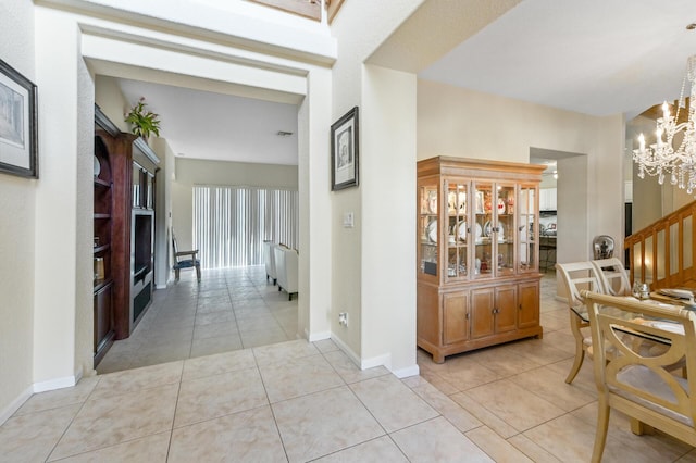 corridor featuring a chandelier, light tile patterned floors, baseboards, and stairs