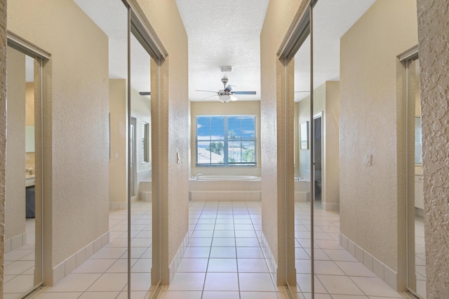 hallway featuring a textured wall, light tile patterned flooring, and a textured ceiling
