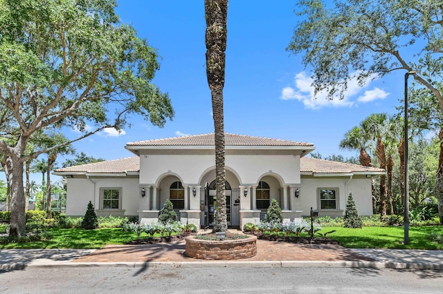 mediterranean / spanish home featuring stucco siding, a tile roof, and a front lawn