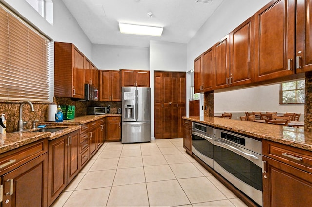kitchen with appliances with stainless steel finishes, a sink, backsplash, light tile patterned flooring, and stone countertops