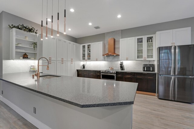 127 Via Castilla, Jupiter, FL 33458 - kitchen featuring appliances with stainless steel finishes, wall chimney range hood, a sink, dark stone countertops, and light wood-style flooring